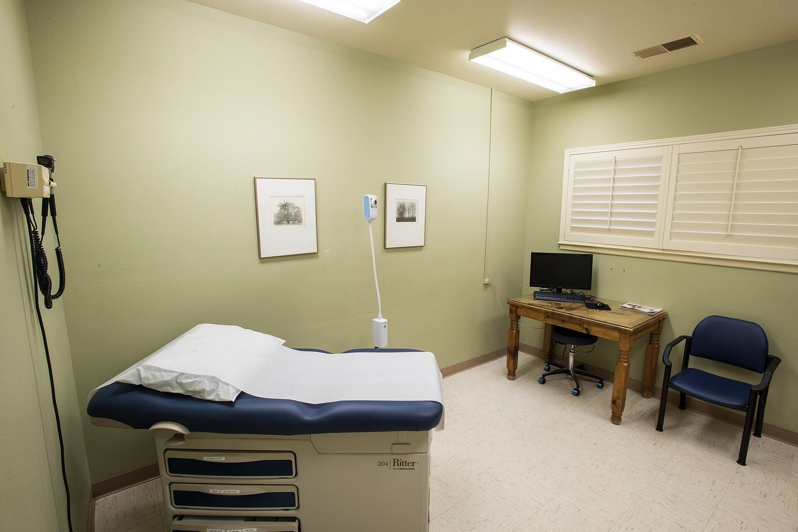 An empty medical examination room with an examination table, desk and chair.